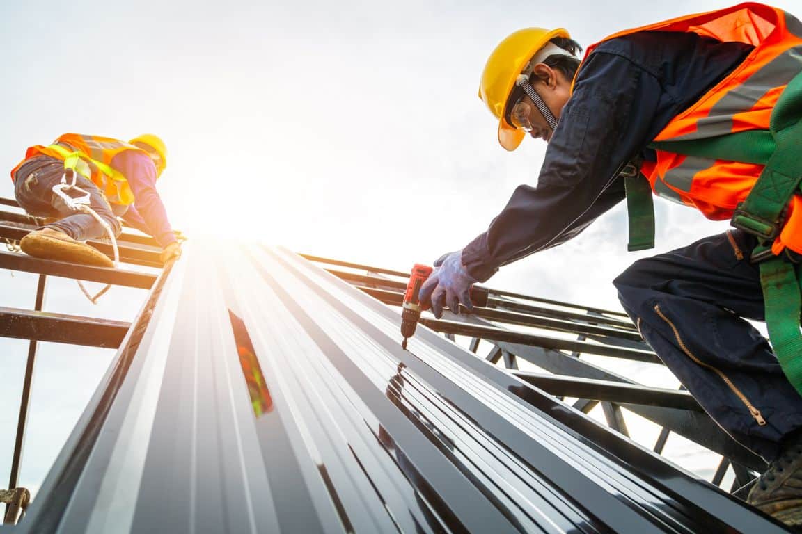 Two workers on a rooftop collaborating on the installation of a metal structure