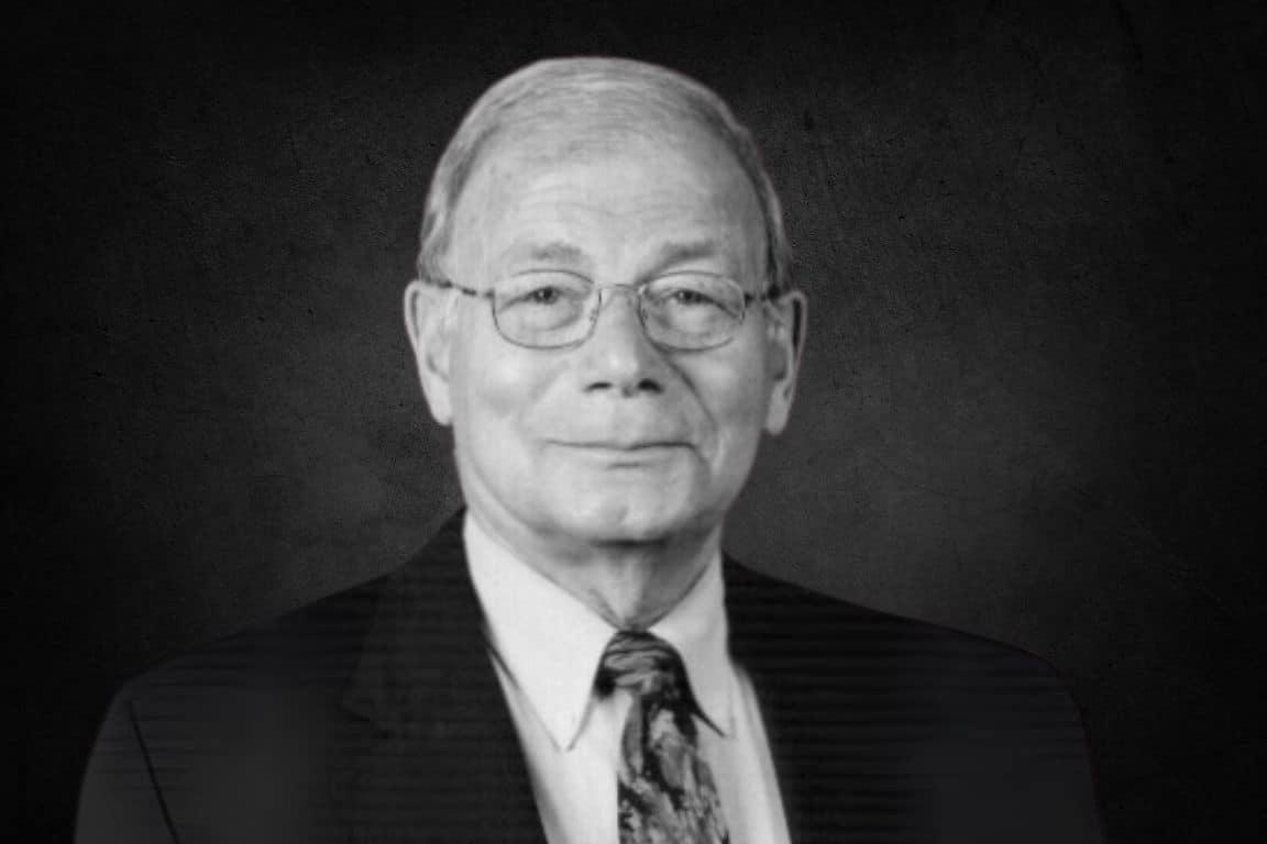 Black and white headshot of a man wearing glasses and professional attire.